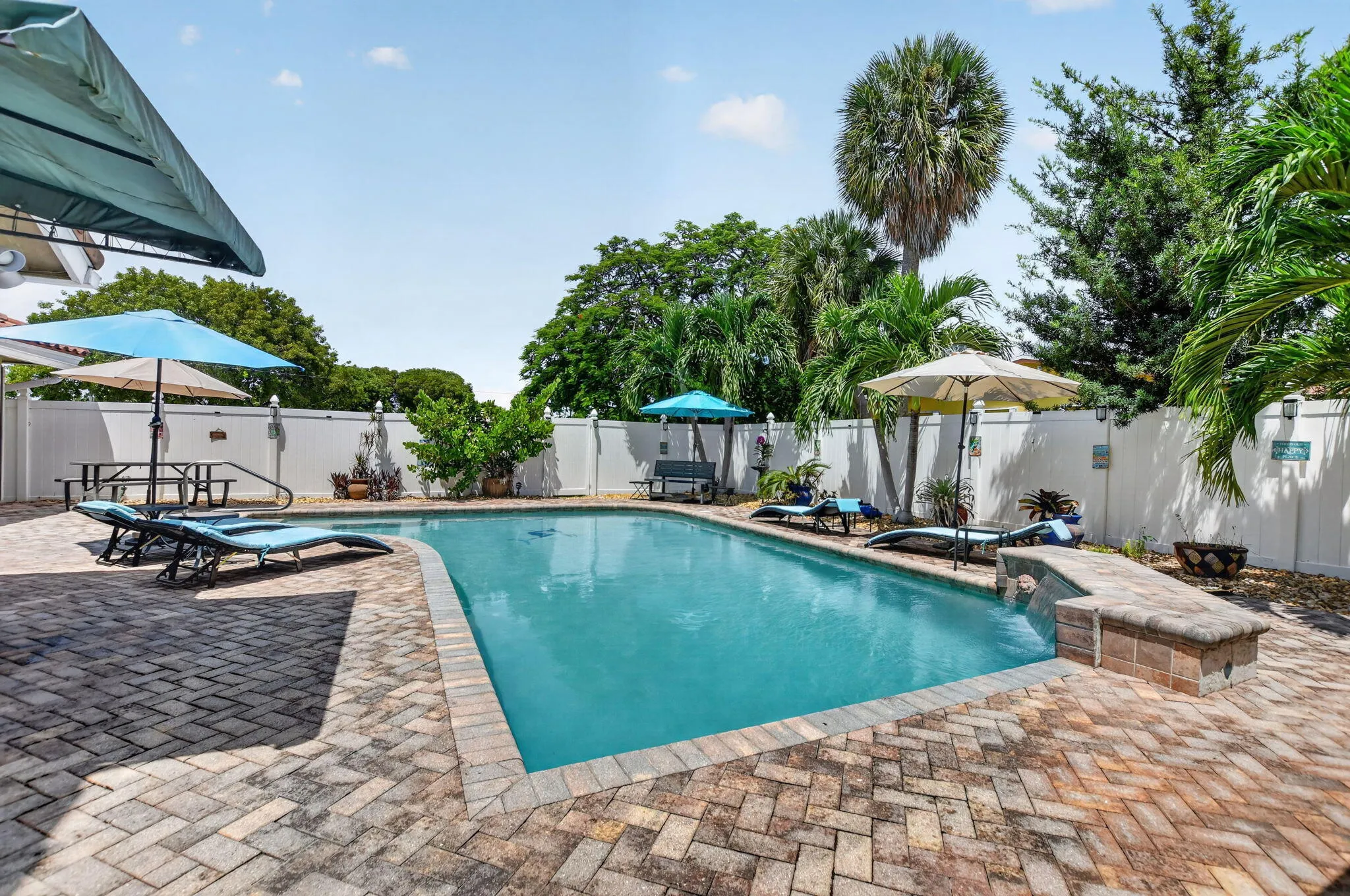 Rectangular swimming pool with a paved brick surround, privacy fencing, and mature landscaping