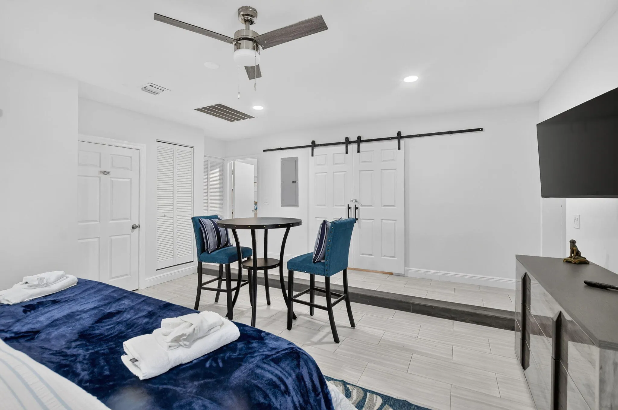 Recessed lighting, ceiling fan, white paneled doors, barn door hardware, and wood-finish flooring