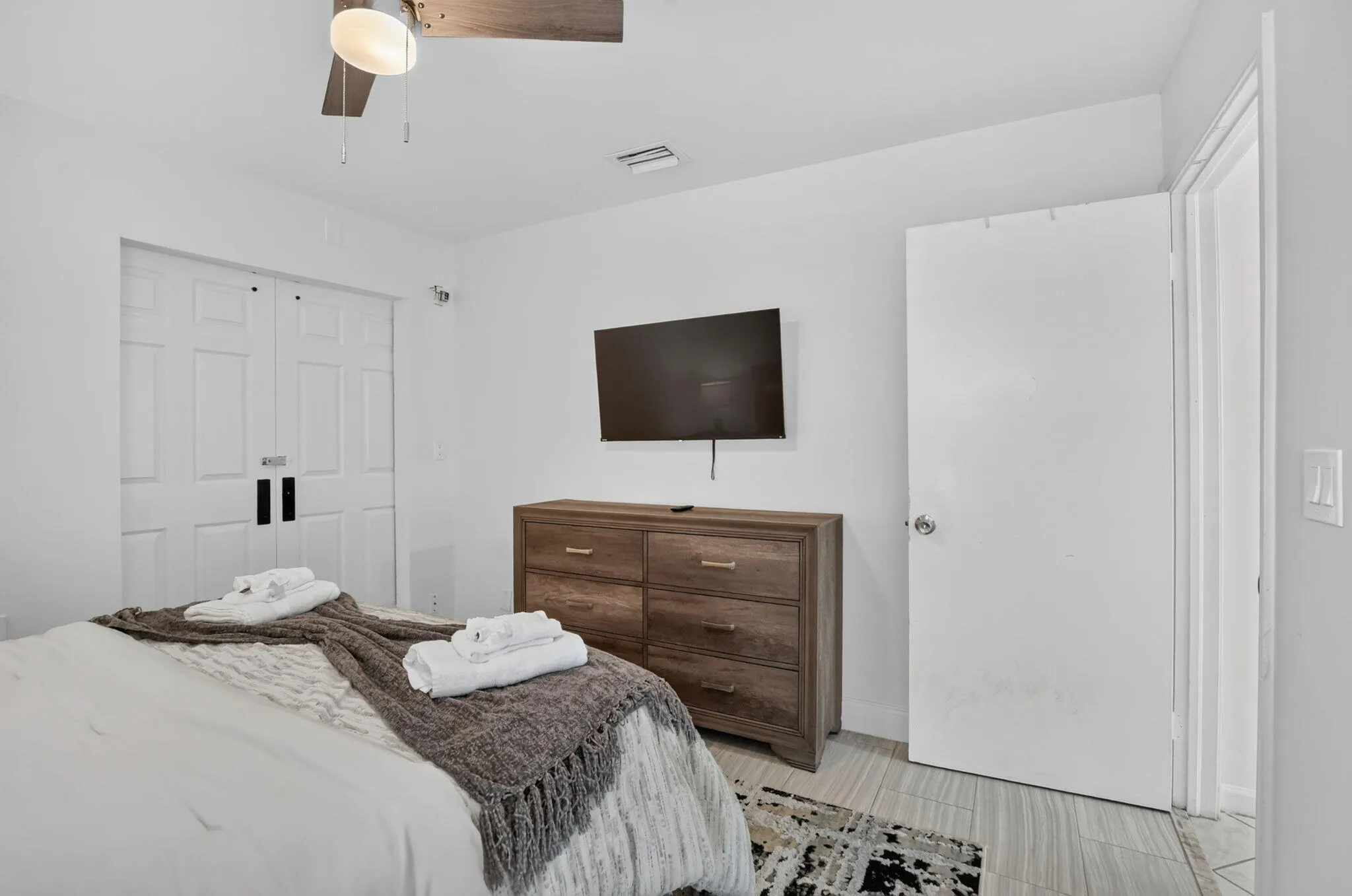 White walls, bi-fold closet doors, wood-finish flooring, and a ceiling fan with light fixture