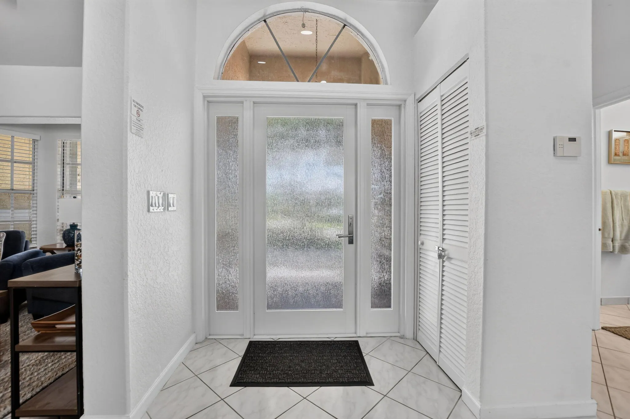Entryway featuring a decorative arched transom window, frosted glass paneled door with side panels, louvered closet doors, and diagonal tile flooring