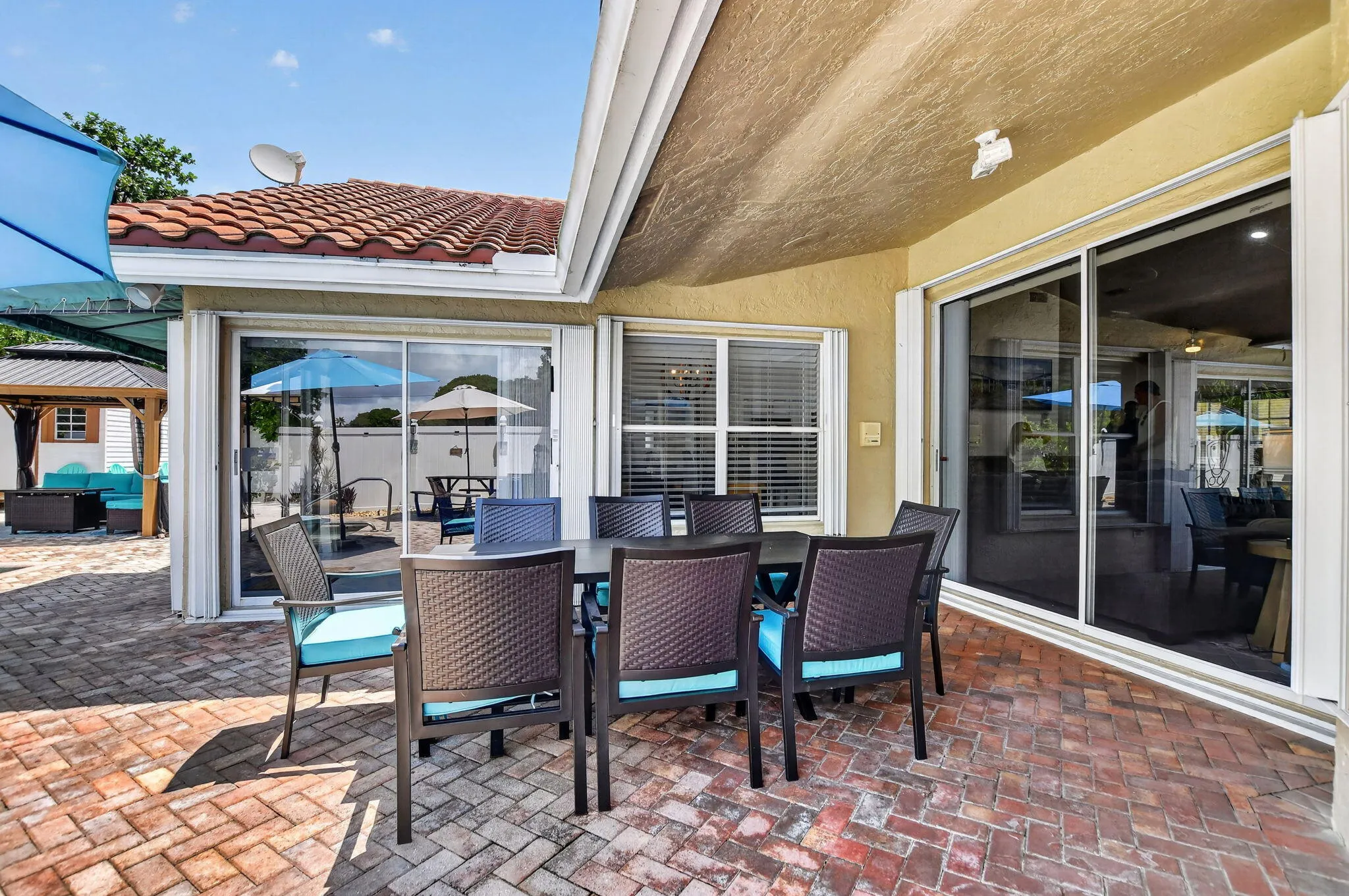 Brick paver patio with a covered dining area, multiple sliding glass doors, and a tile roof