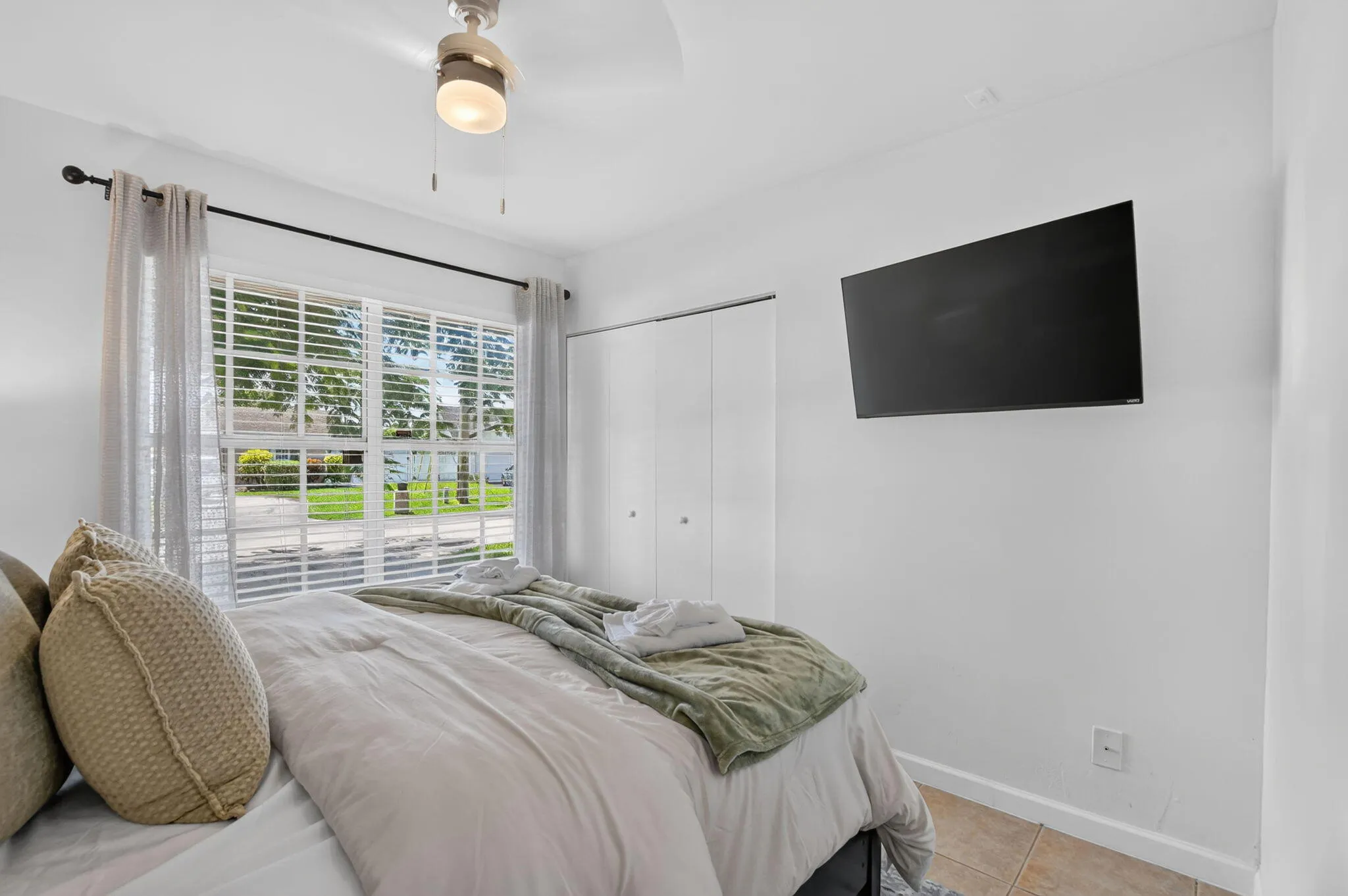 Window with horizontal blinds, ceiling fan with integrated lighting, wall-mounted television, and bi-fold closet doors