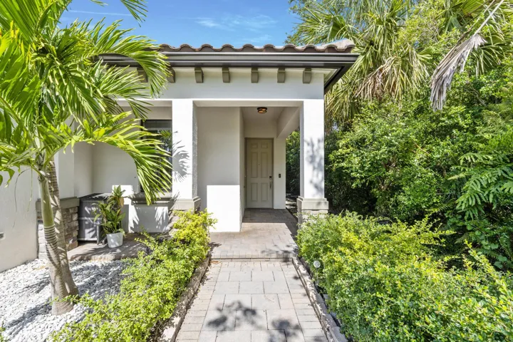 Modern architectural entry featuring a clean-lined white facade with deep overhanging eaves, framed by mature tropical landscaping including palms and lush greenery