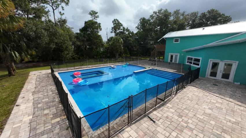 Expansive outdoor swimming pool featuring an integrated spa, safety fencing, and tiered entry steps