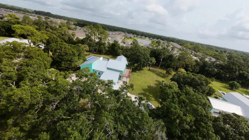 Expansive green space featuring a vibrant turquoise exterior, multiple mature trees, and a spacious deck
