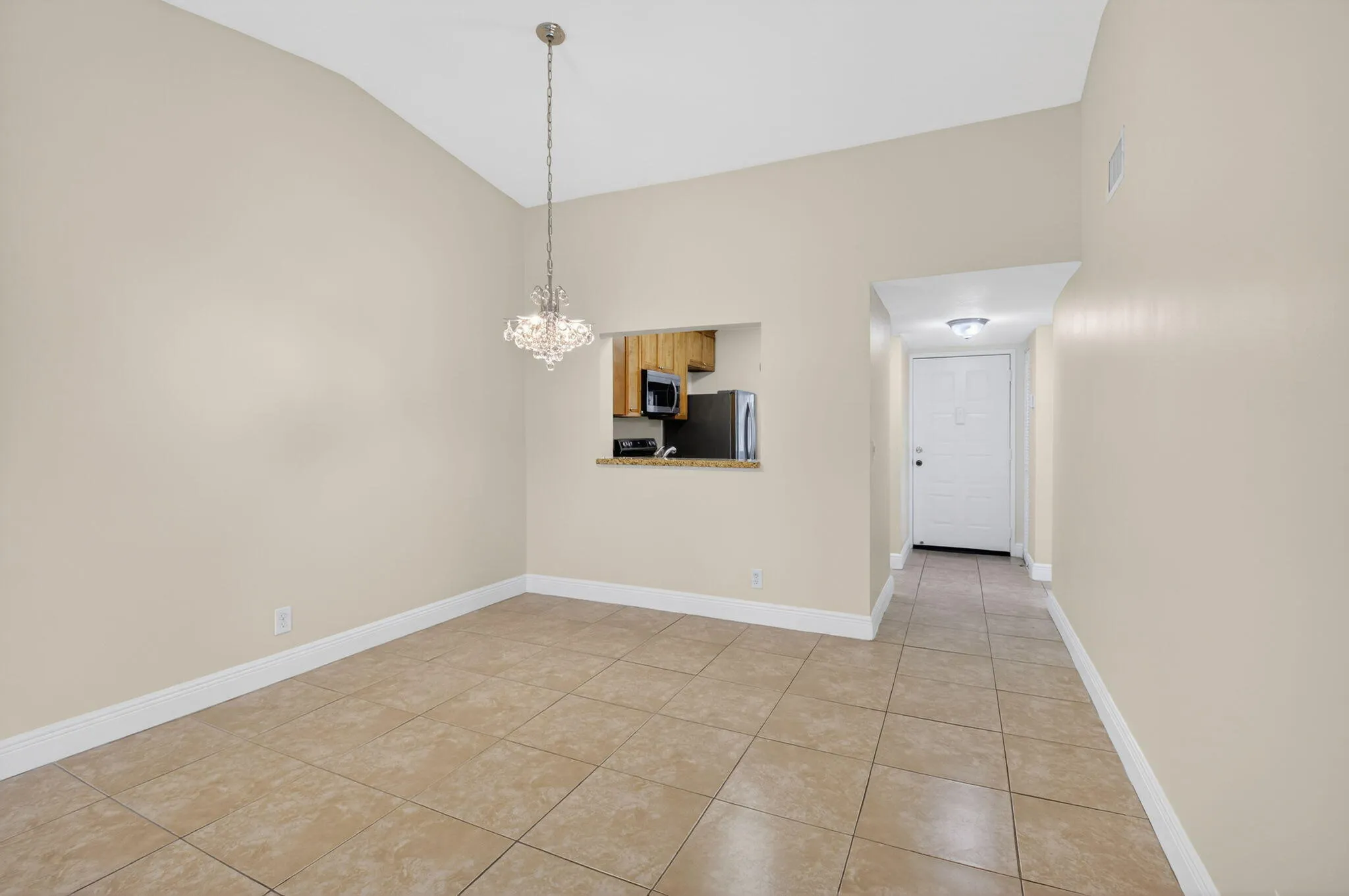Vaulted ceiling, crystal chandelier, tile flooring, kitchen pass-through, and entry door
