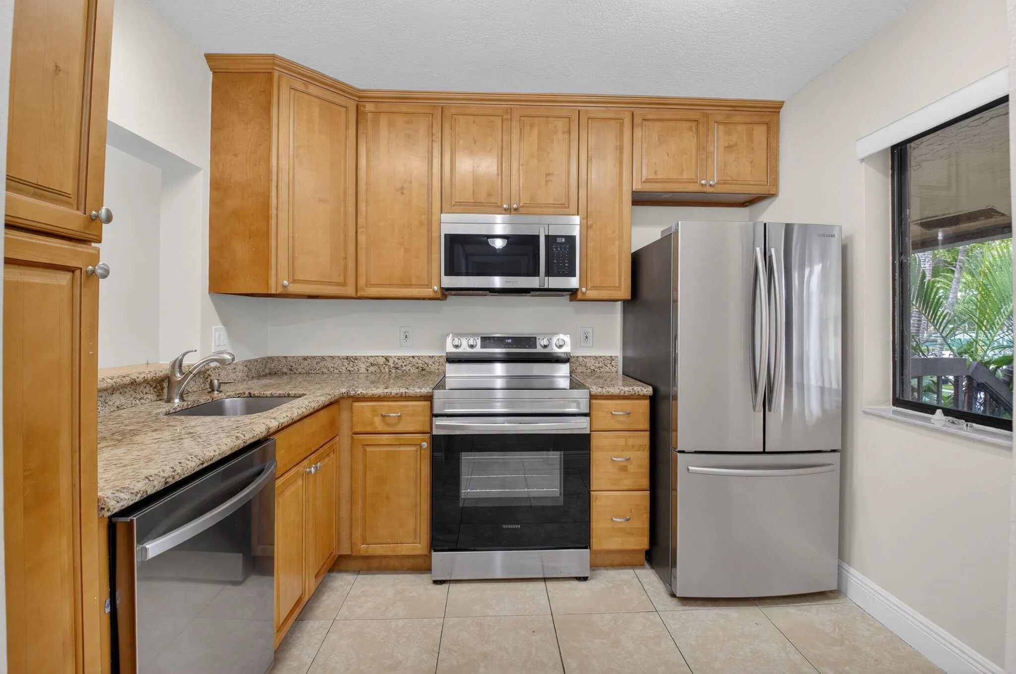 Kitchen featuring wood cabinetry, stainless steel appliances, a corner sink with a gooseneck faucet, and a stone-finish countertop