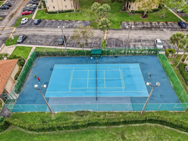 Tennis court with blue surfacing, surrounded by fencing and green landscaping