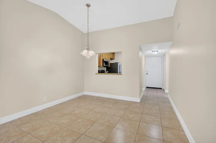 Vaulted ceiling, crystal chandelier, tile flooring, kitchen pass-through, and entry door