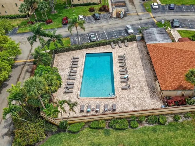 Rectangular swimming pool with a stone paver deck, surrounded by mature landscaping and a low privacy wall