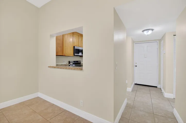 Tile flooring throughout, kitchen pass-through with stone-finish countertop, wood cabinetry, and stainless steel microwave