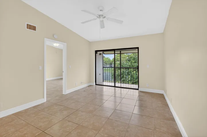 Tiled flooring, white ceiling fan, sliding glass door, black balcony railing, and neutral wall paint