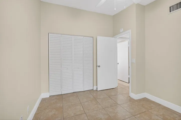 Spacious bedroom featuring tile flooring, louvered closet doors with glass panel entry door, and neutral wall finishes throughout