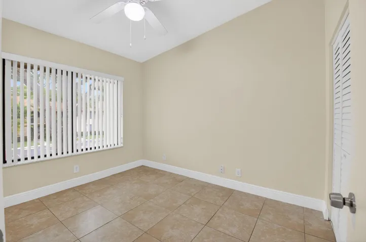 Tiled flooring, vaulted ceiling, ceiling fan, window with vertical blinds, and a louvered door