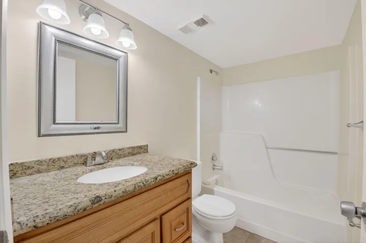 Bathroom featuring a wood-finish vanity with a granite-style countertop, undermount sink, and a framed mirror