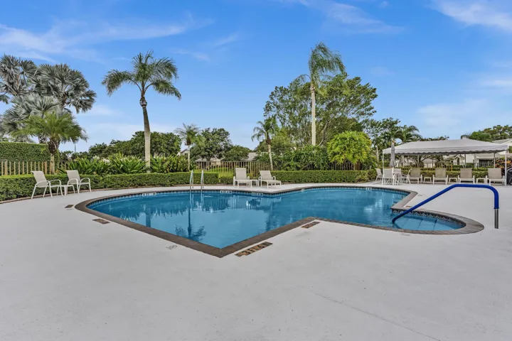 Kidney-shaped swimming pool with an integrated spa, surrounded by a light-colored paved deck and lush landscaping