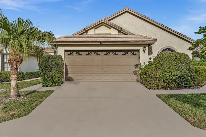 Stucco exterior with a tiled roof, featuring an arched window, a two-car garage with decorative inserts, and established landscaping