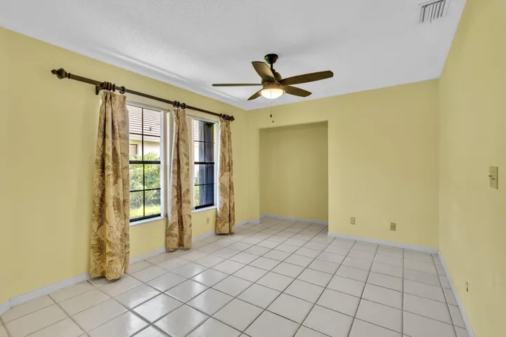 Tiled flooring throughout, two windows, crown molding, ceiling fan with integrated lighting, and a recessed entryway