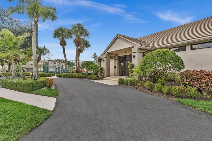 Building exterior with a tiled roof, mature tropical landscaping, paved driveway, and an entryway with double doors