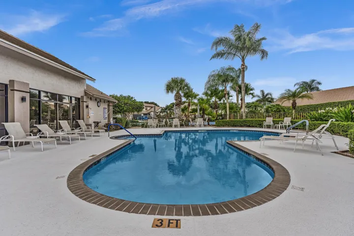 Shaped swimming pool with a brick coping, surrounded by a light-colored paved deck, and tropical landscaping