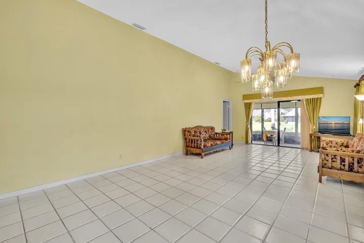 Tiled flooring, vaulted ceiling, multi-pane sliding glass door, and a decorative chandelier