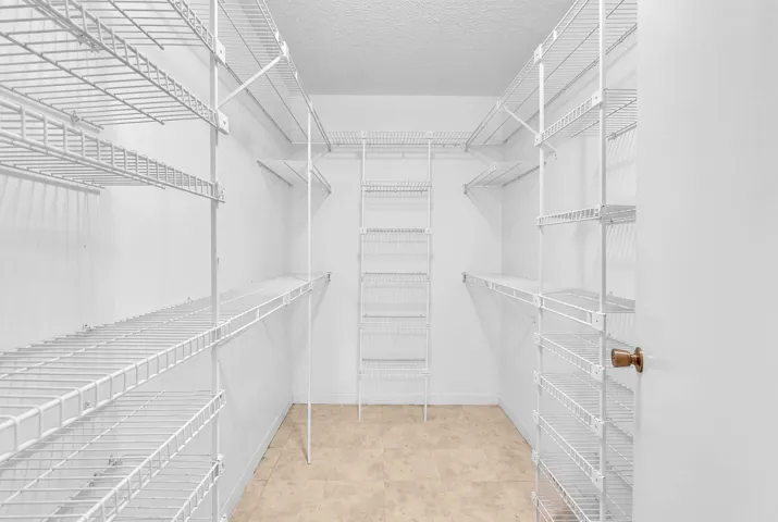 Walk-in closet featuring white wire shelving, multiple storage levels, and a light-toned tile floor