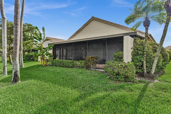 Screened patio with exterior wall sconces, surrounded by manicured landscaping and mature palm trees