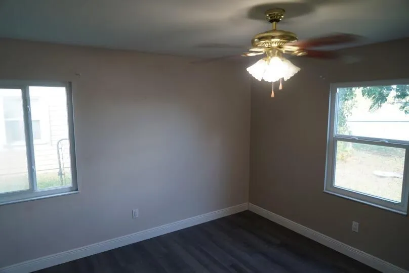 Wood-finish flooring with white trim, two windows, and a ceiling fan with integrated lighting