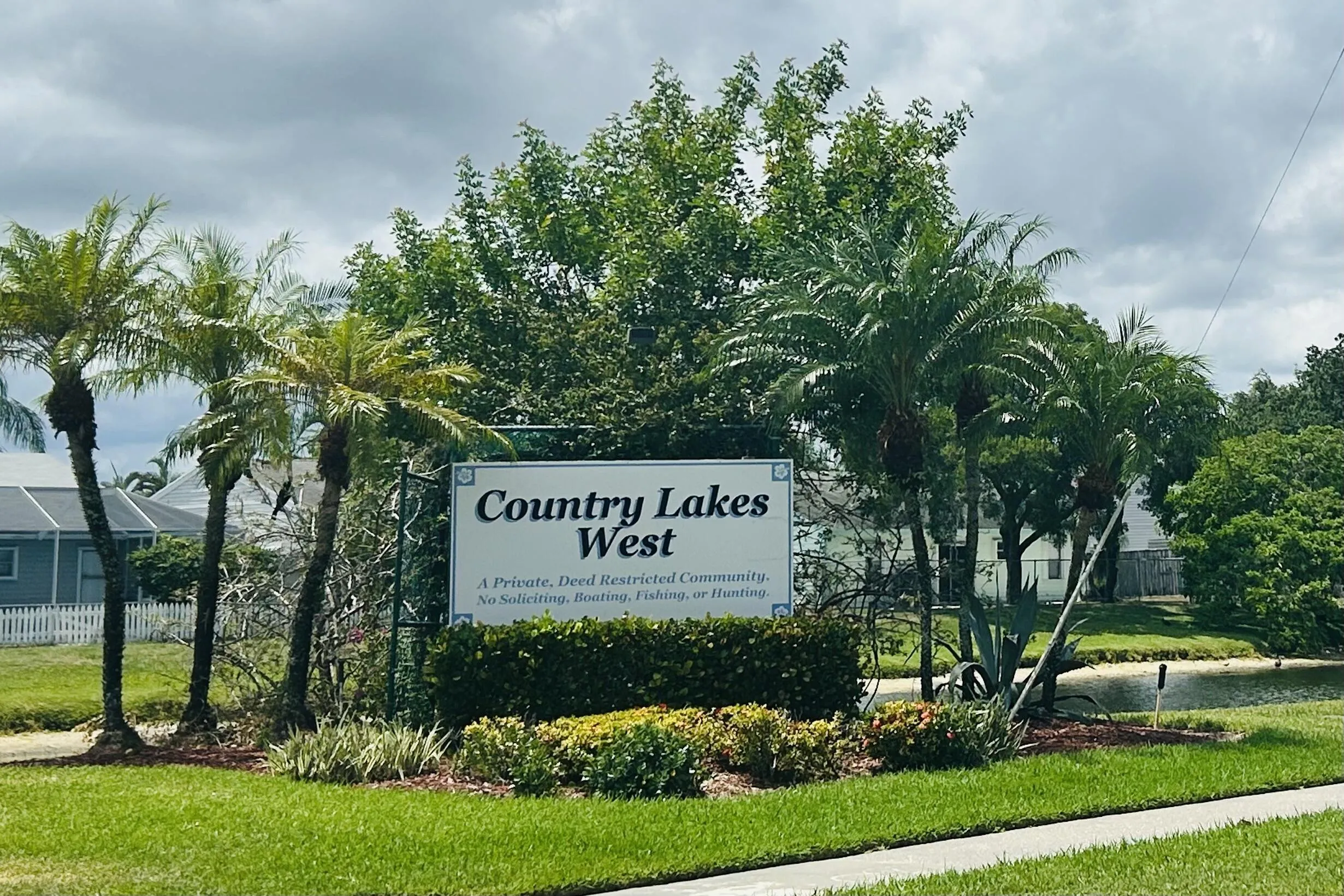 Community entrance signage featuring established landscaping, mature palm trees, and a manicured lawn