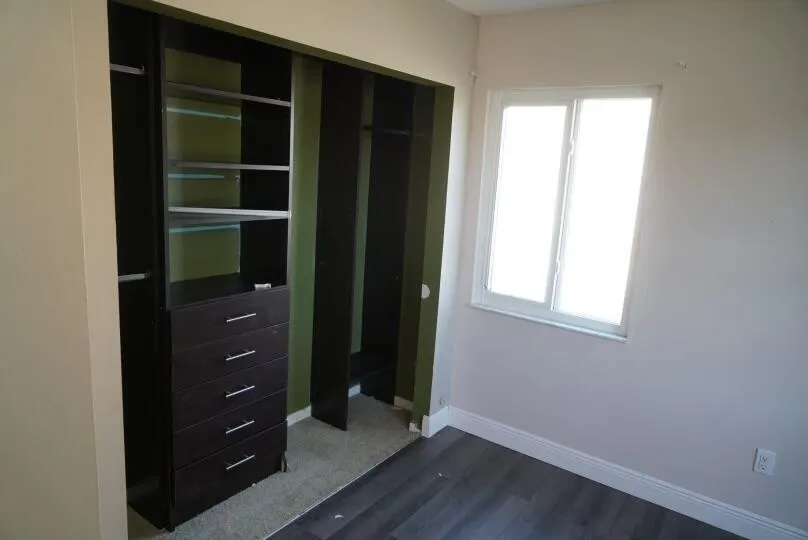 Custom closet organization system featuring shelving and drawers, accompanied by a window with white trim and wood-finish flooring