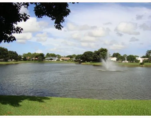 Expansive lake with a central water feature, surrounded by lush green landscaping and a residential backdrop