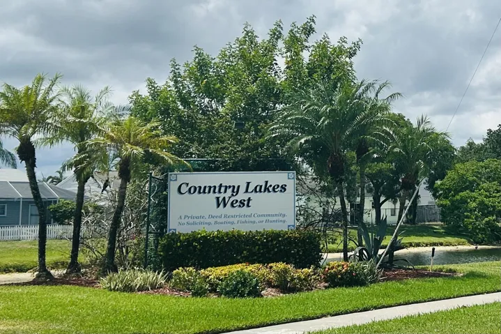 Community entrance signage featuring established landscaping, mature palm trees, and a manicured lawn