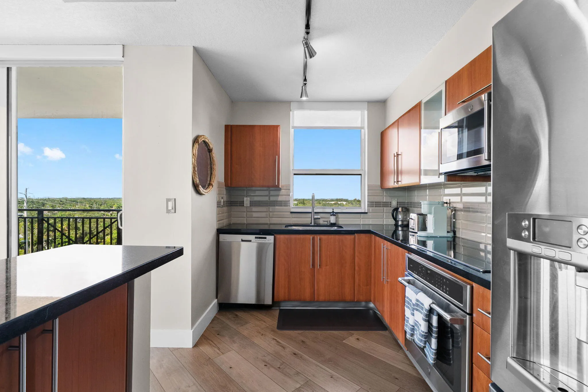 Alternate kitchen view showcasing generous cabinetry, stainless steel appliances, window over the sink & direct terrace access.