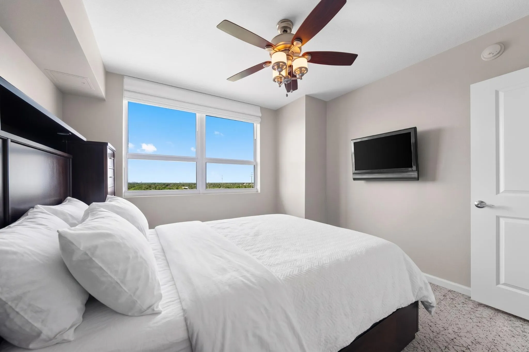 Alternate view of the furnished second bedroom with wall-mounted television, large window & comfortable guest accommodations.