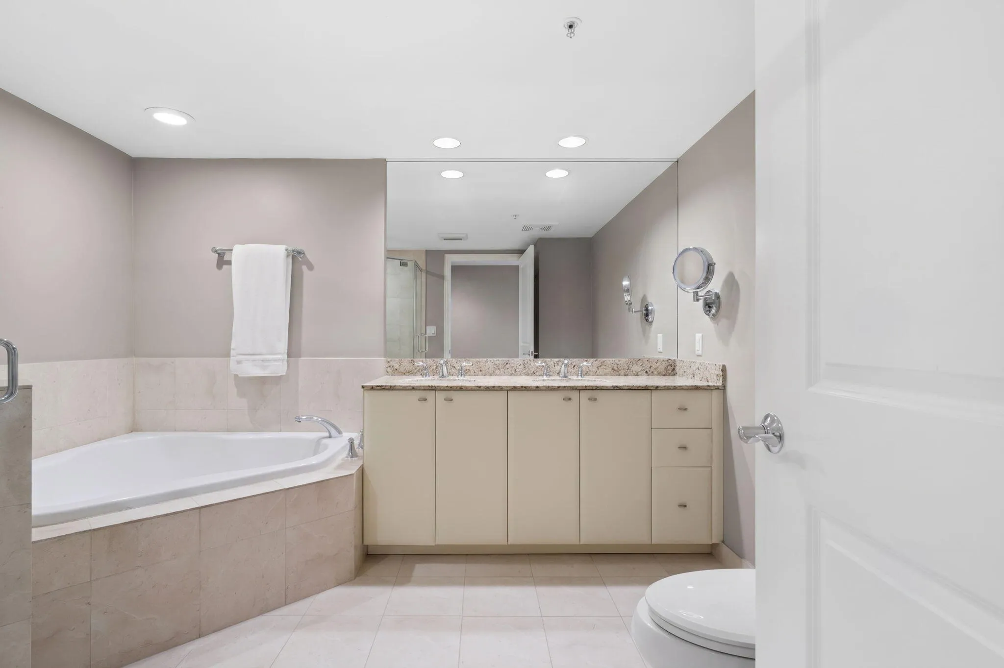 Spa-like primary bathroom with dual granite vanities, oversized soaking tub, large mirror & abundant cabinet storage.