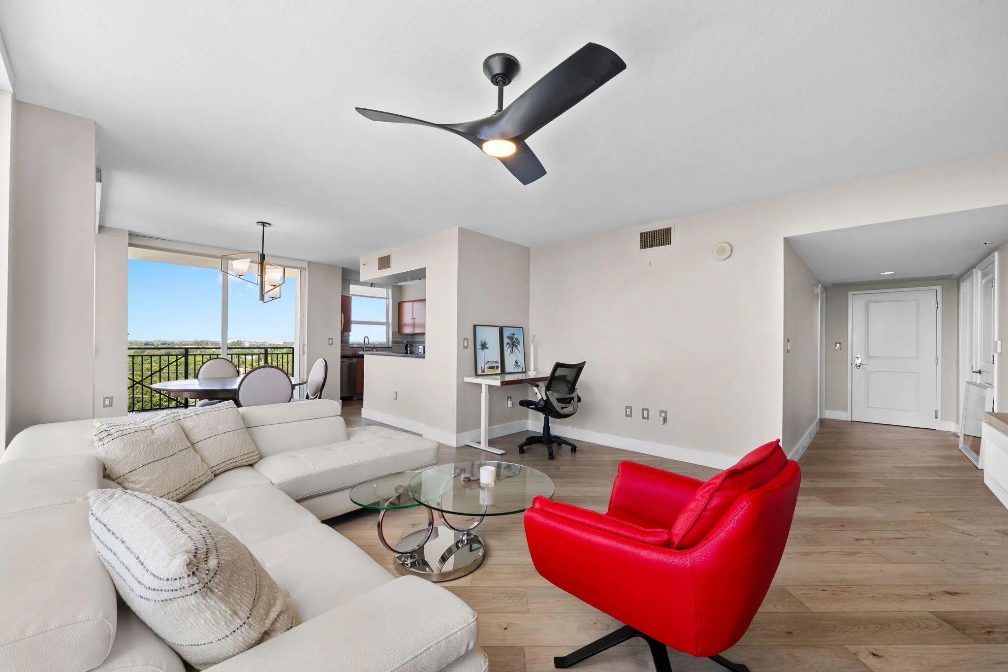 Wide view of the open living & dining areas, featuring a dedicated desk/workstation, modern furnishings & an easy connection to the kitchen and terrace.