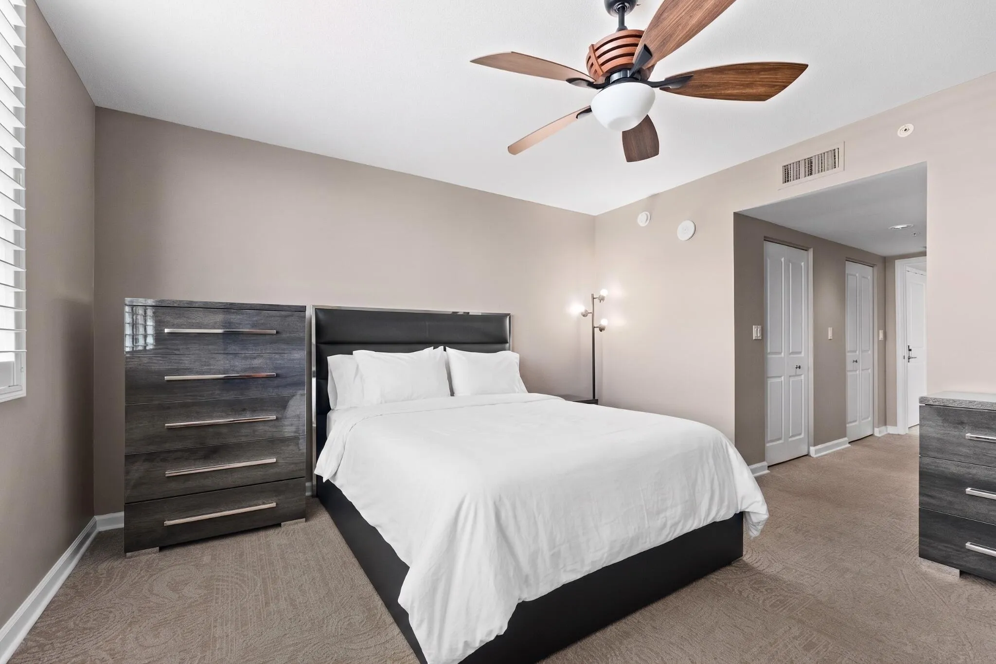 Furnished primary suite with bed, matching dressers, ceiling fan & convenient access to the primary bath and walk-in closets.