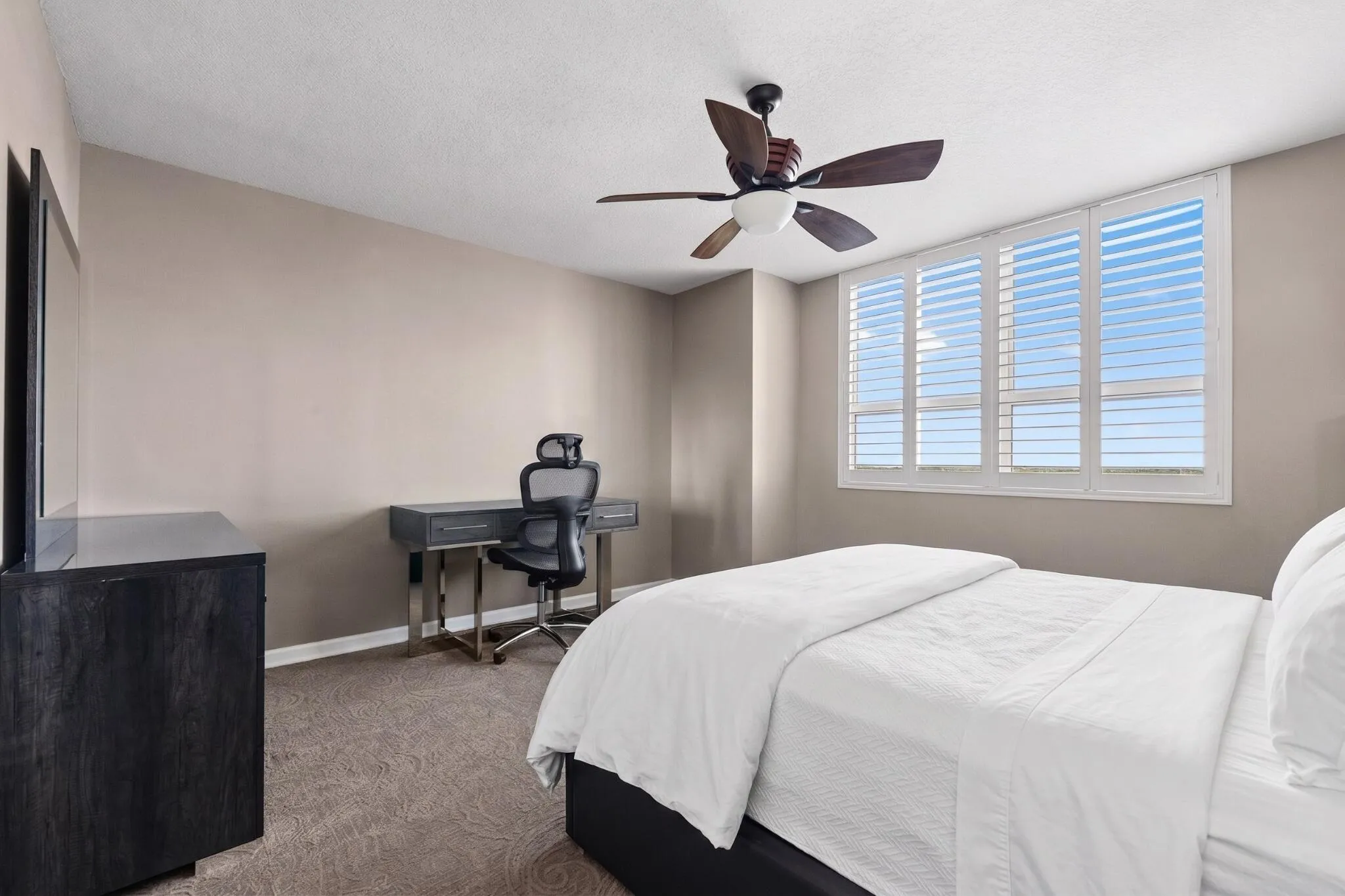Alternate view of the spacious primary bedroom, featuring plantation shutters, dedicated desk/workstation, dresser & generous natural light.