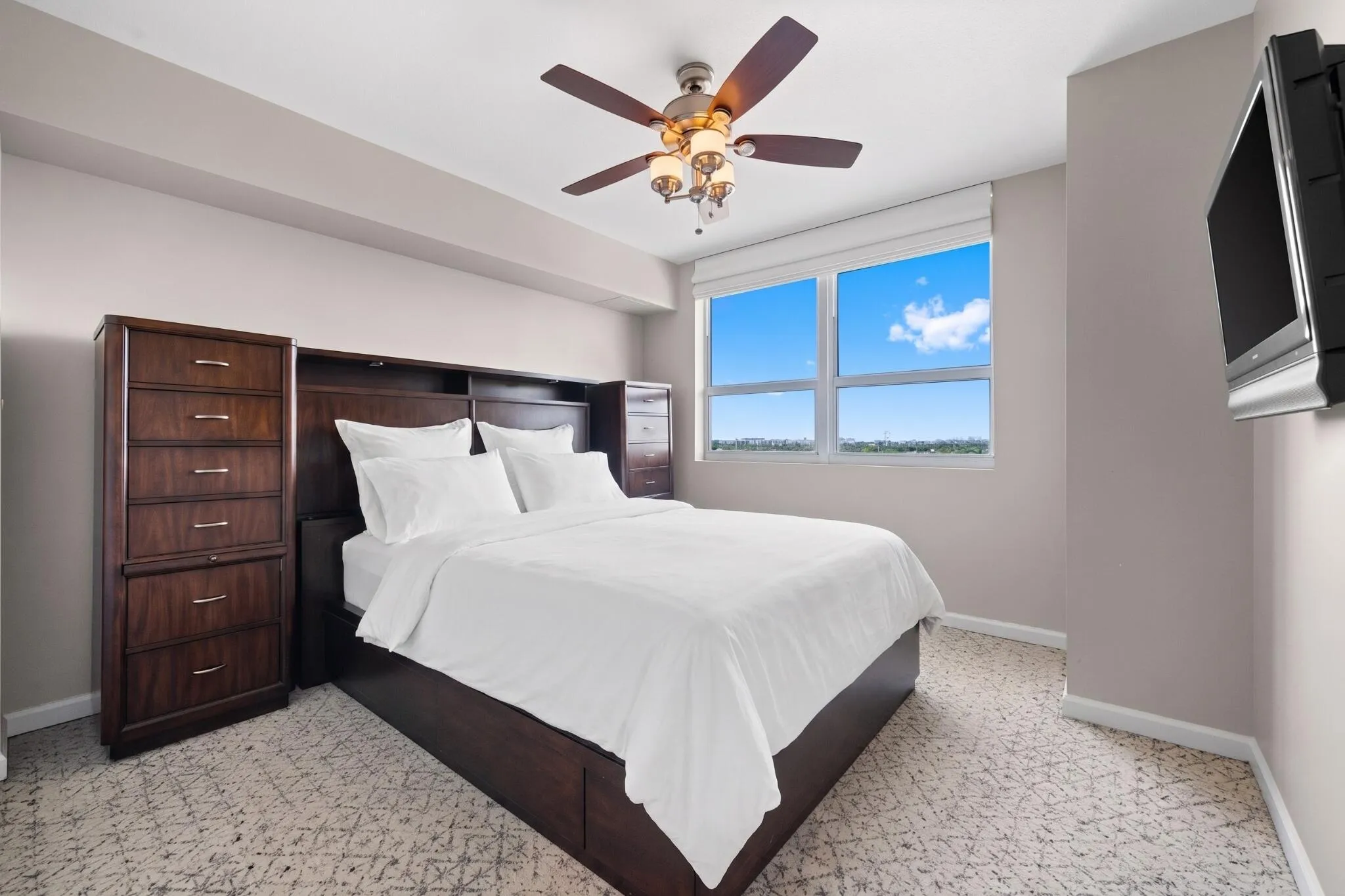 Furnished second bedroom with bed, built-in storage cabinetry, television, ceiling fan & large window with open views.
