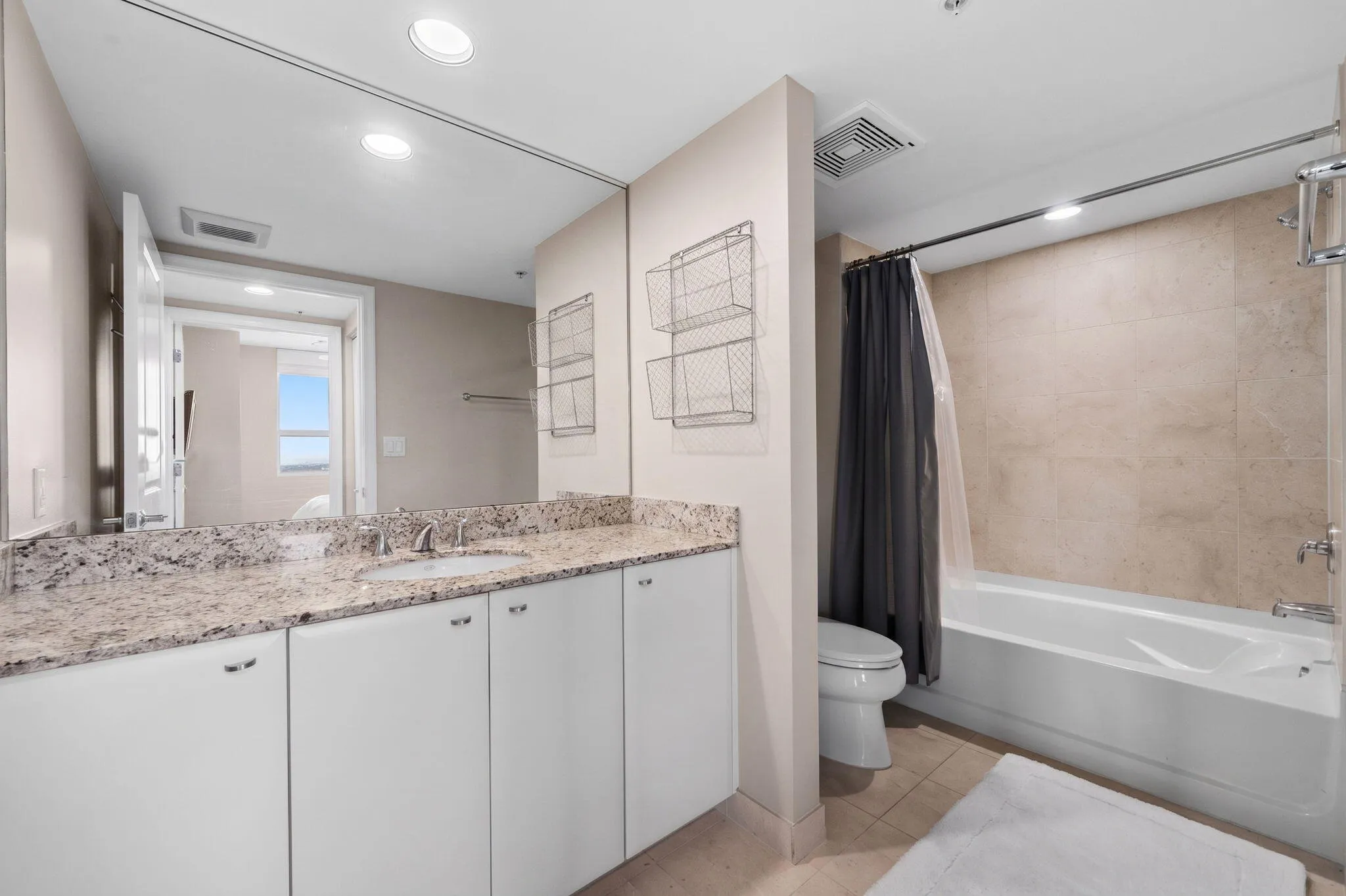 Second full bathroom with granite vanity, large mirrored wall & tub/shower combination with neutral tile surround.