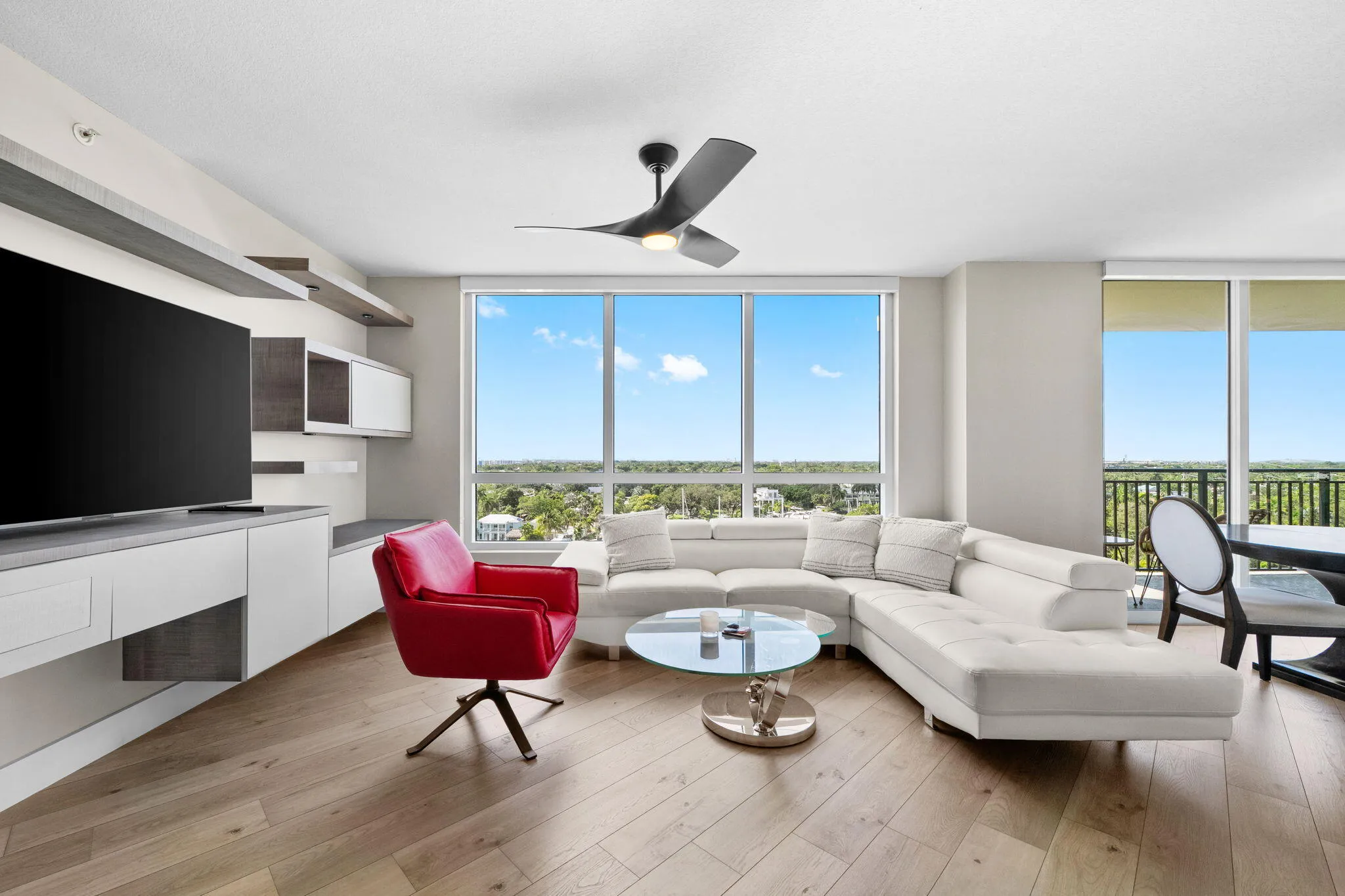 Spacious furnished living room with a large sectional sofa, accent chair, custom built-in media wall & broad southwest views across Fort Lauderdale.