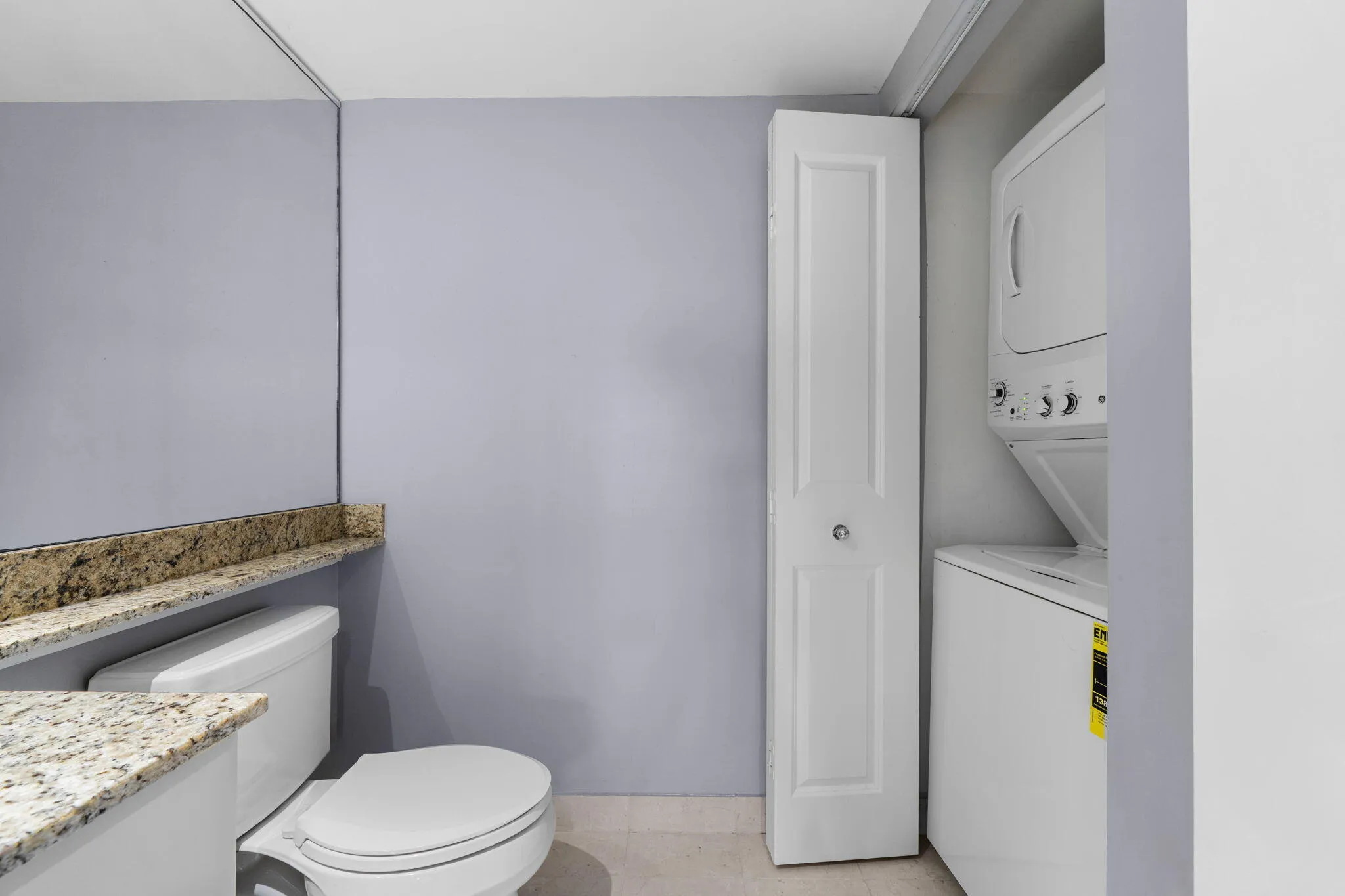 Alternate view of the powder room showing the granite counter, mirrored wall & adjacent in-unit laundry closet.