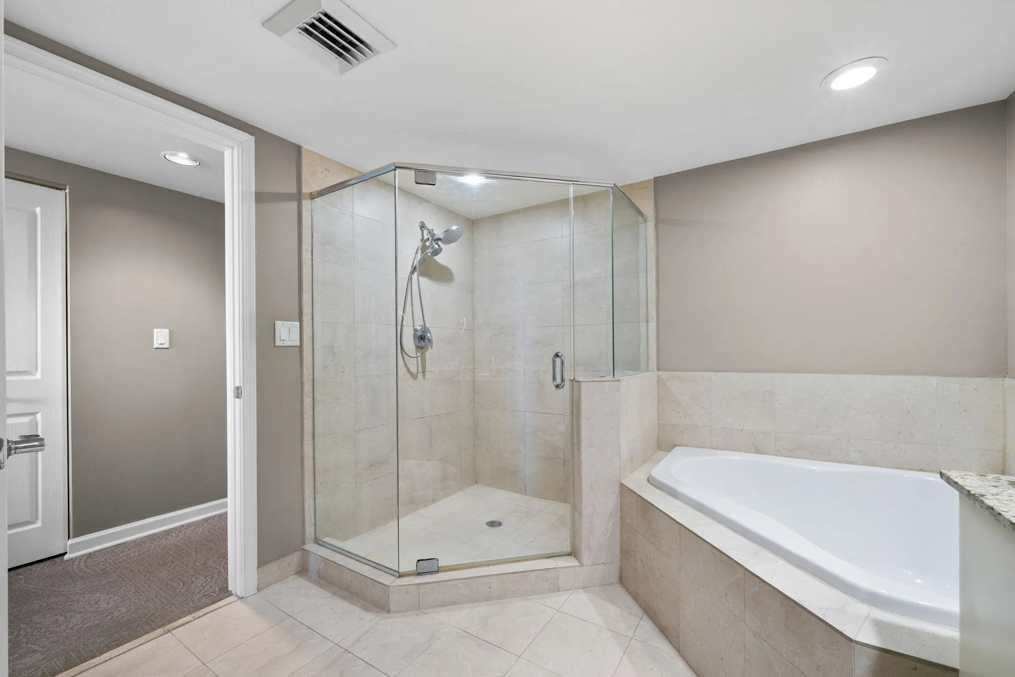 Primary bath featuring a separate glass-enclosed walk-in shower, oversized soaking tub & neutral tile finishes.