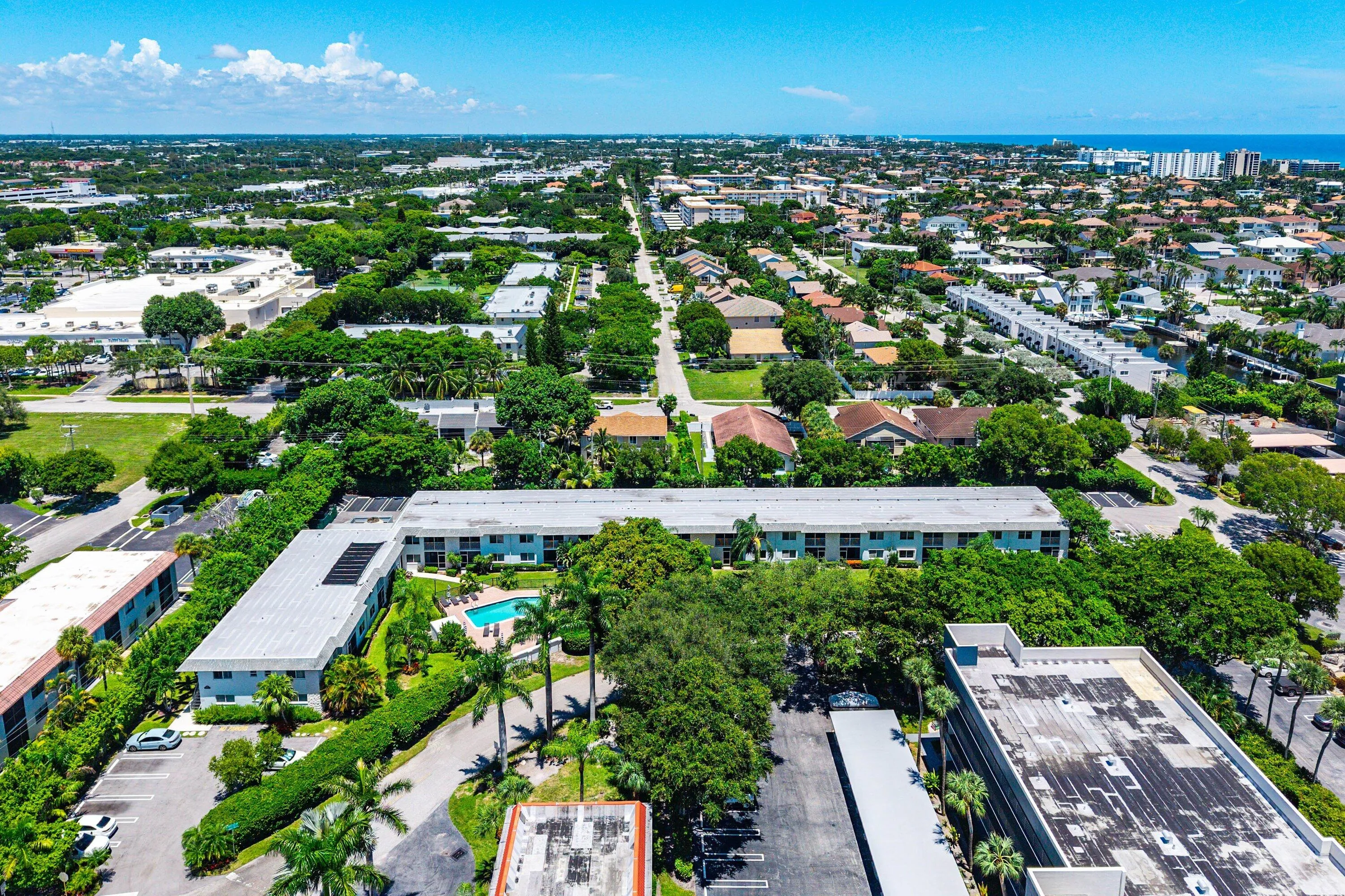 Aerial perspective of residential buildings with an outdoor swimming pool, surrounded by mature trees and paved parking areas
