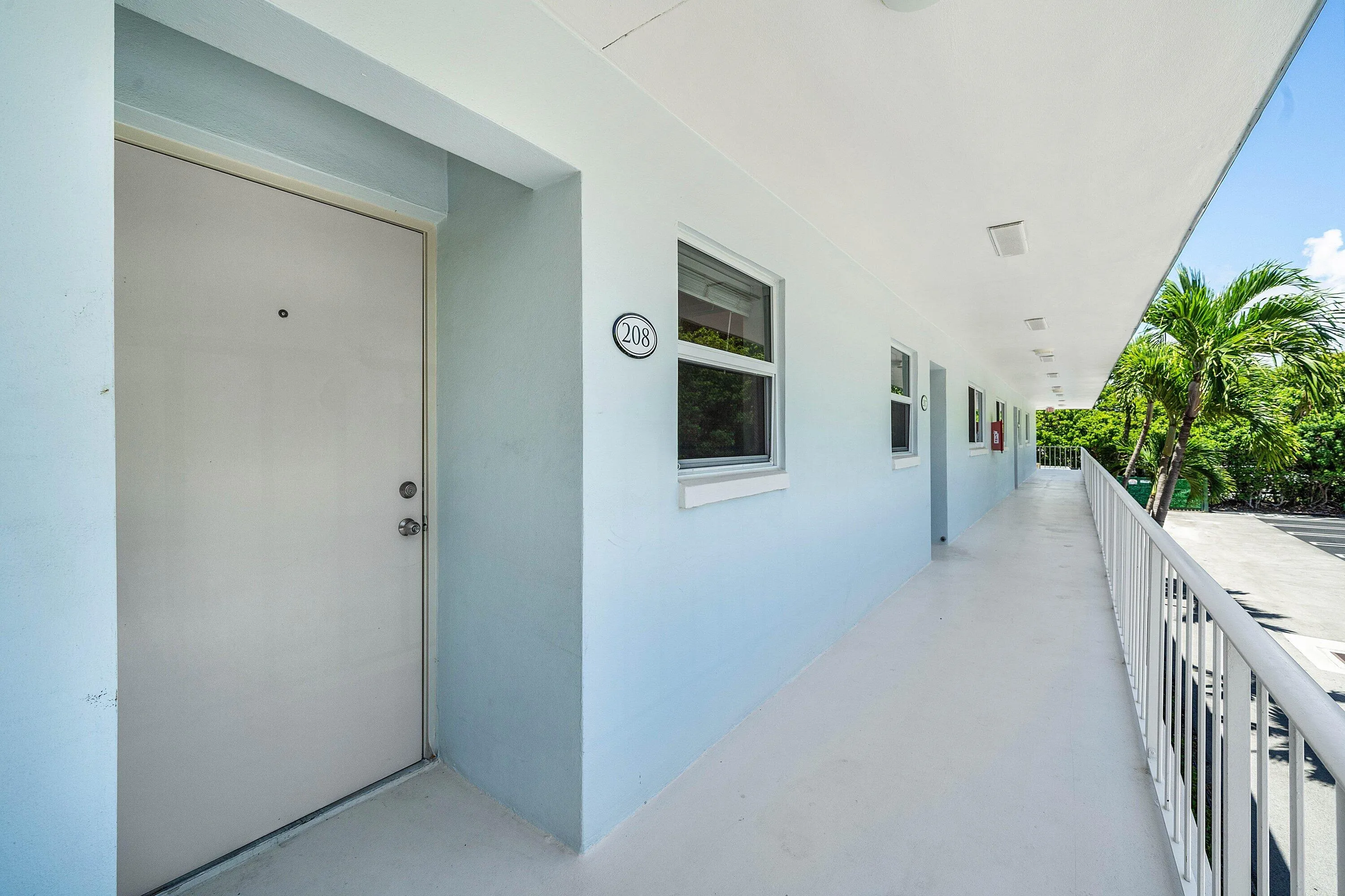 Exterior walkway featuring light blue walls, white railing, and multiple windows