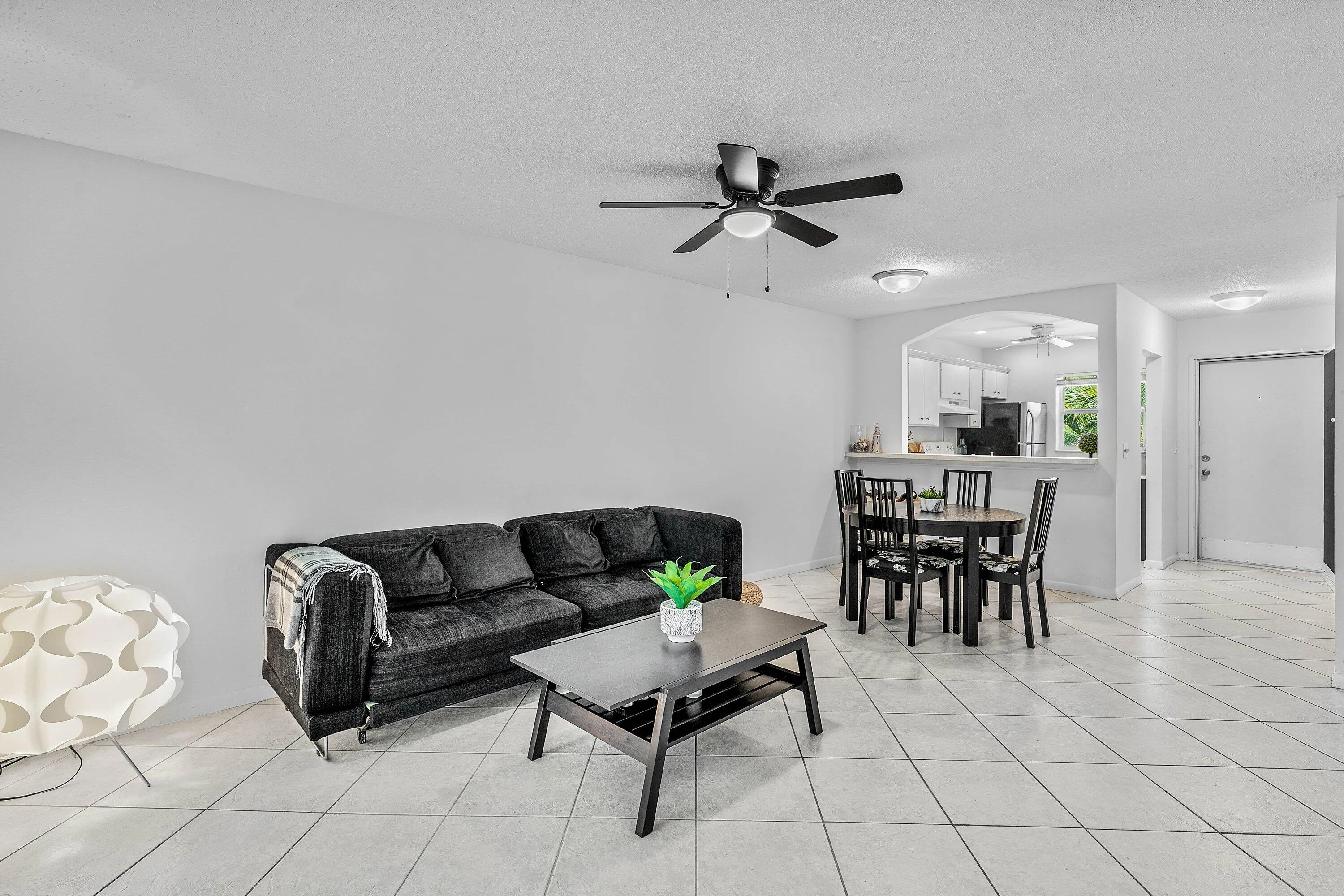 Open-concept living area featuring tile flooring, ceiling fan with integrated lighting, and an arched pass-through to the kitchen
