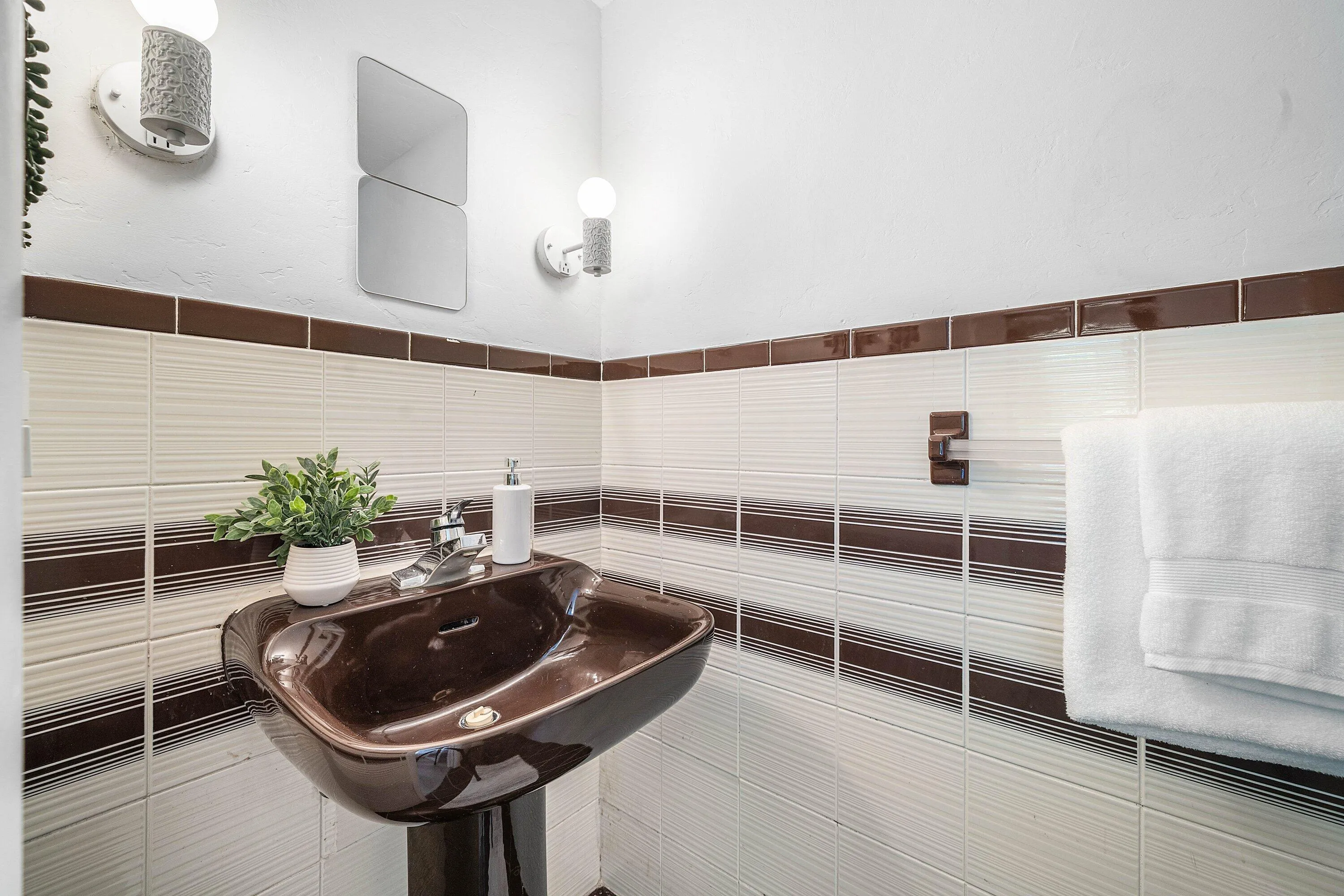 Pedestal sink with a dark brown finish, white and brown tiled wall, and wall-mounted light fixtures