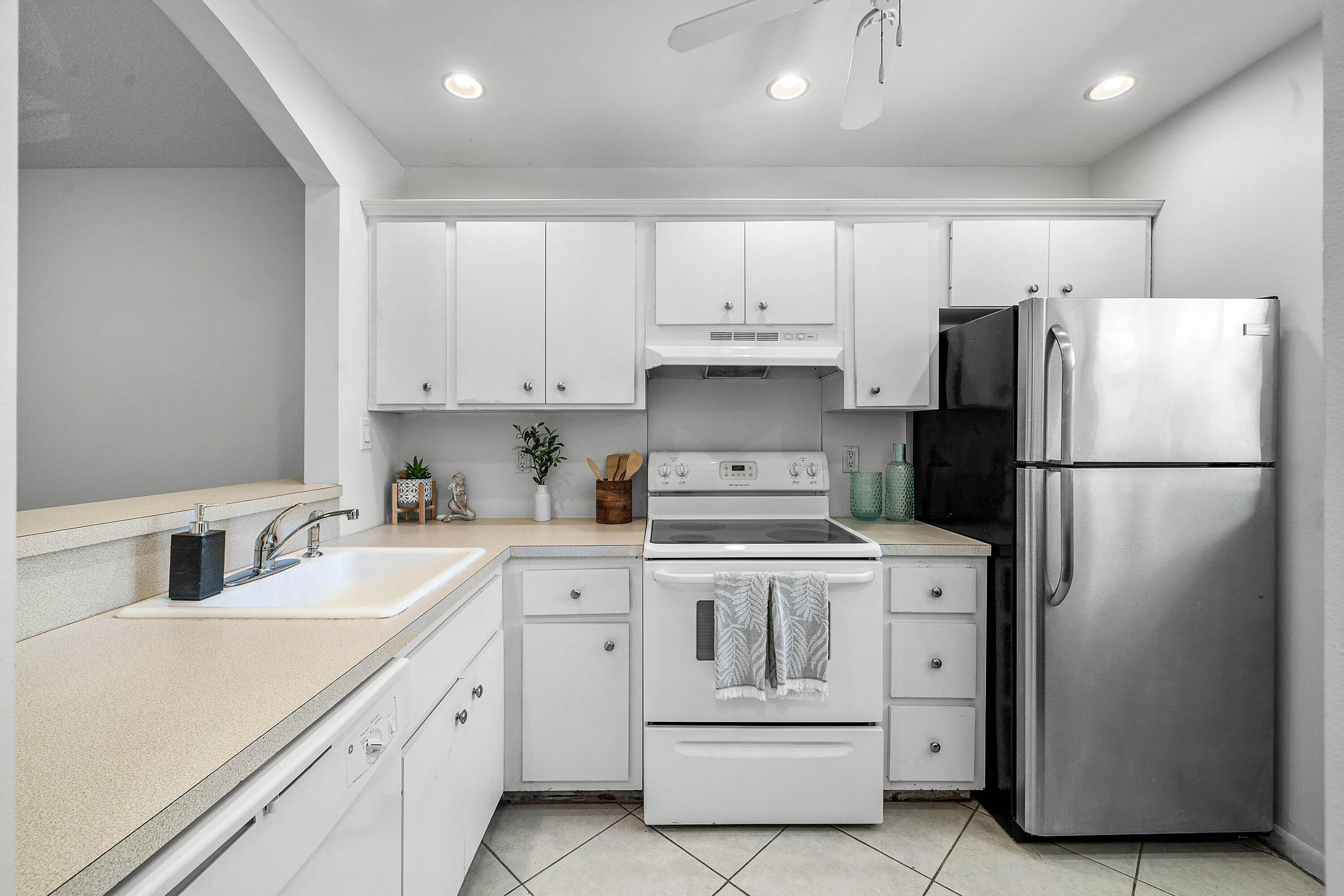 White cabinetry, light-toned countertops, white tile flooring, and a stainless steel refrigerator