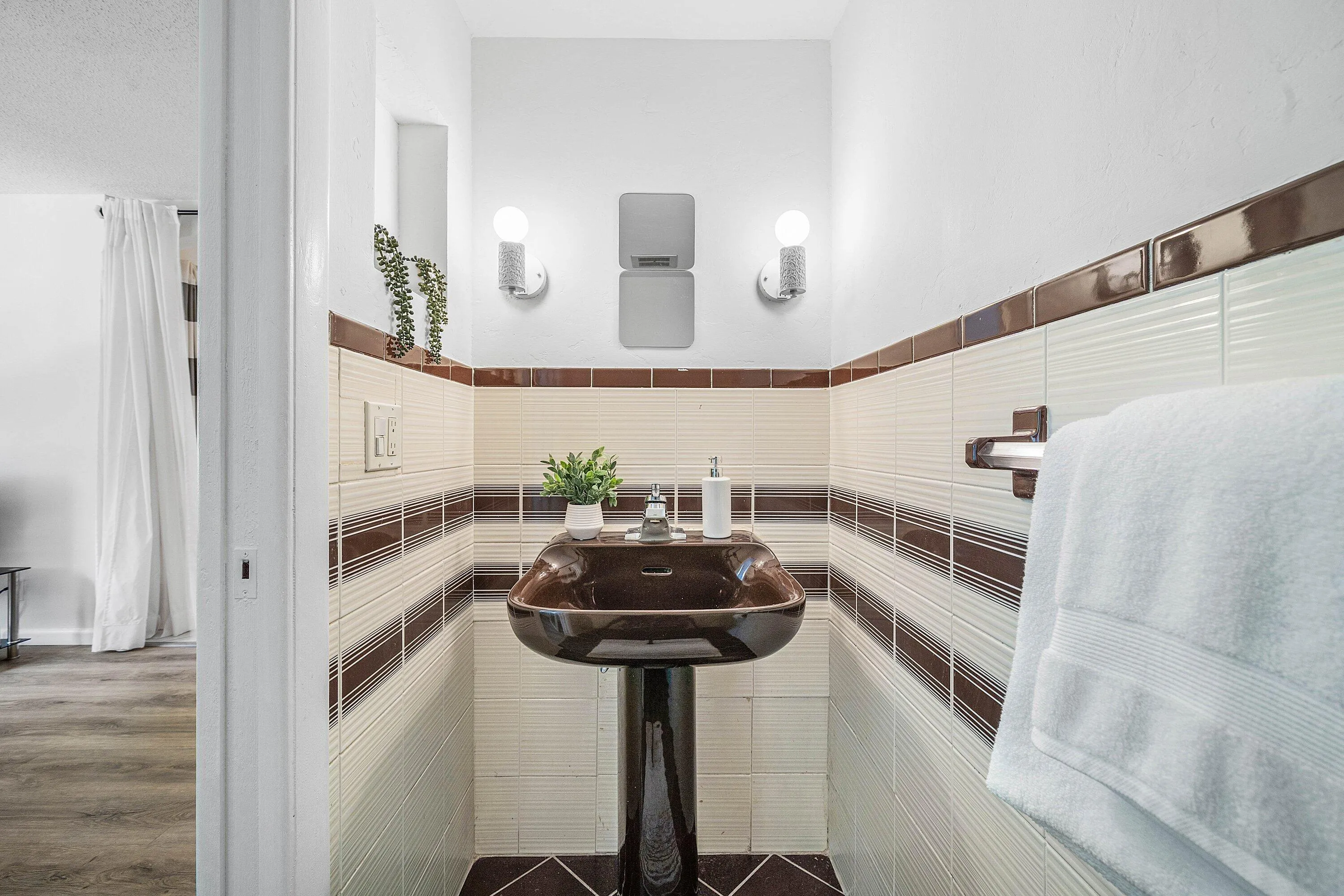 Pedestal sink, wall-mounted light fixtures, tiled walls with decorative banding, and tile flooring