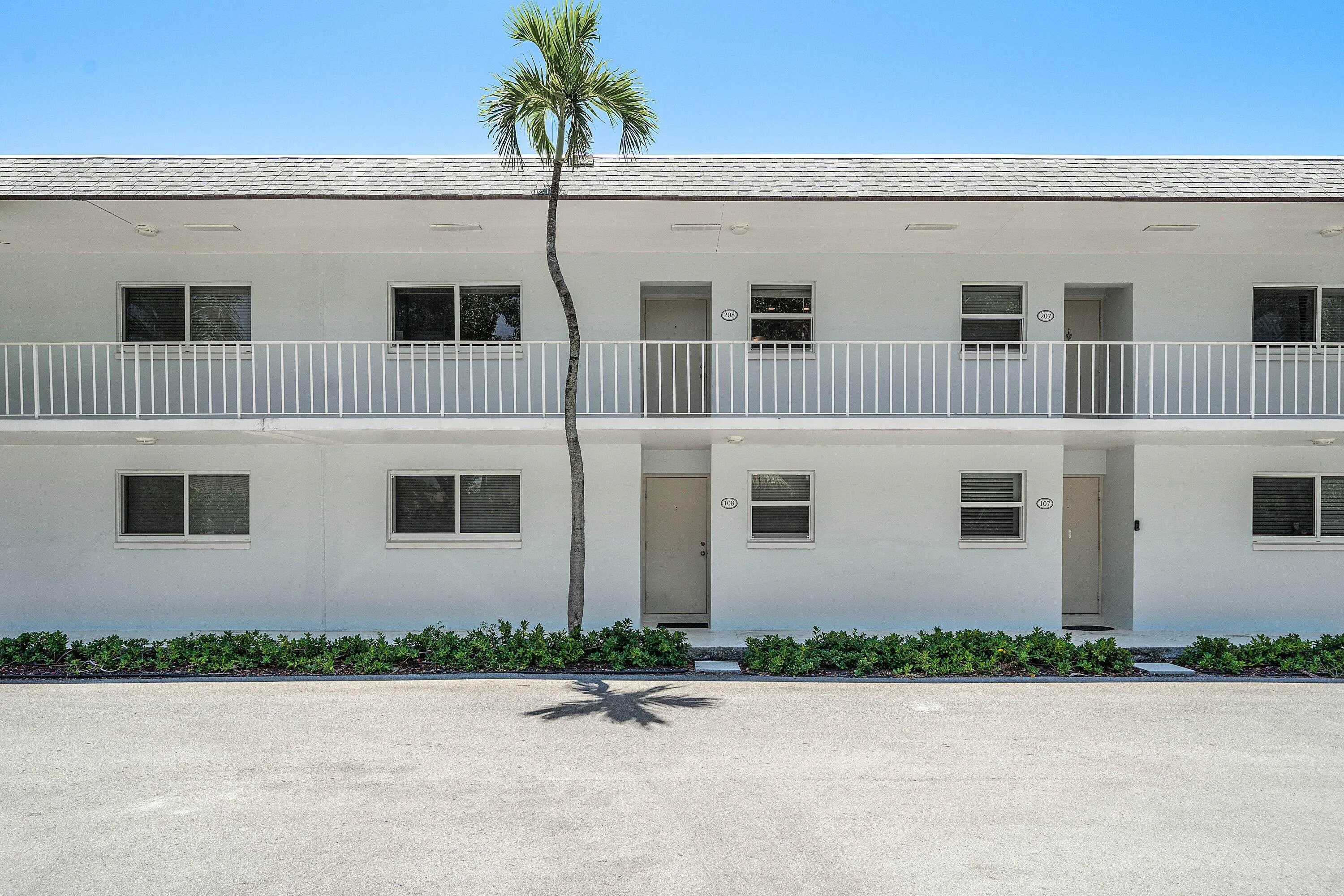 Two-story facade with white exterior, white balcony railings, and ground-level landscaping